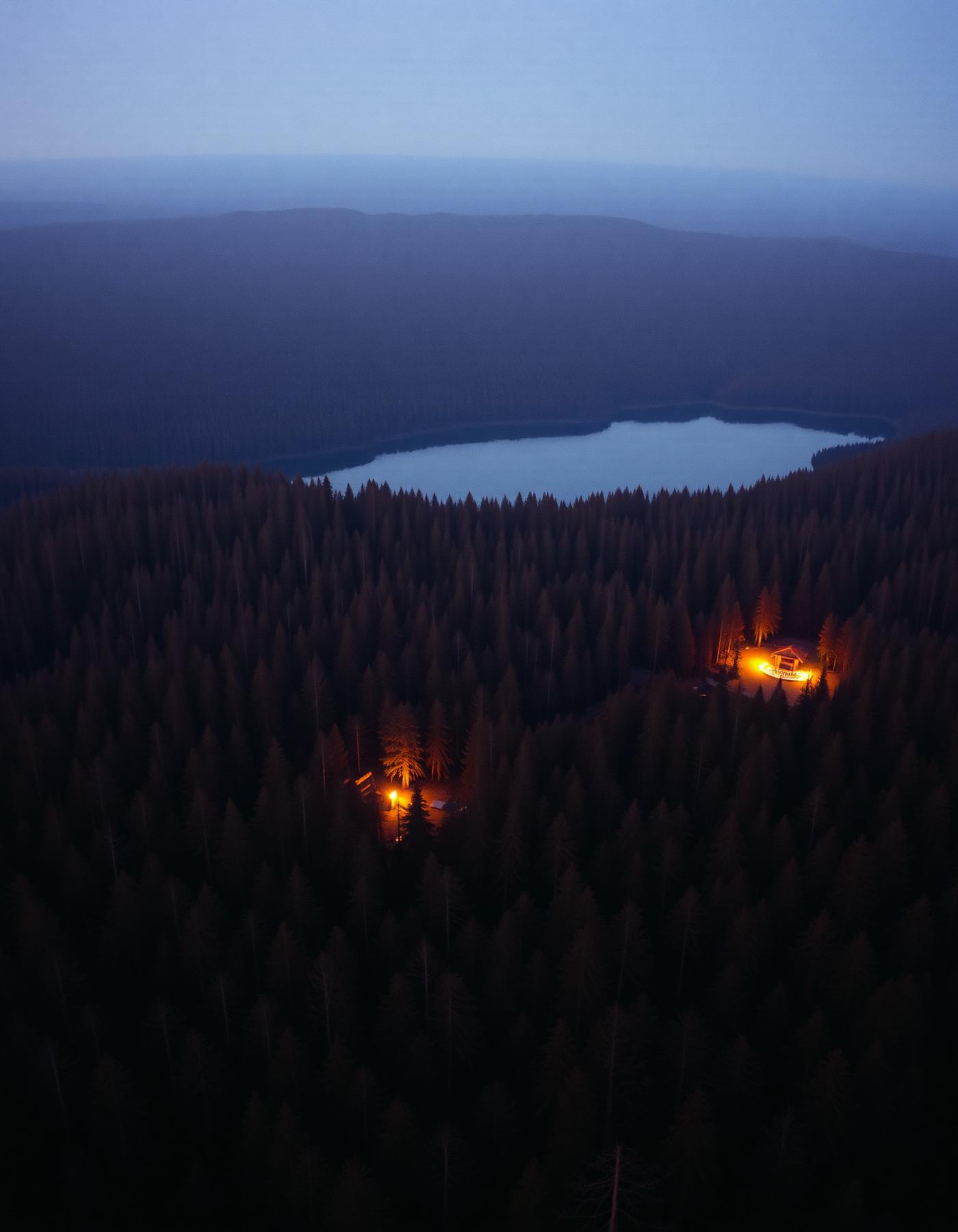 Aerial dusk view of forest and lake with lantern-lit camps