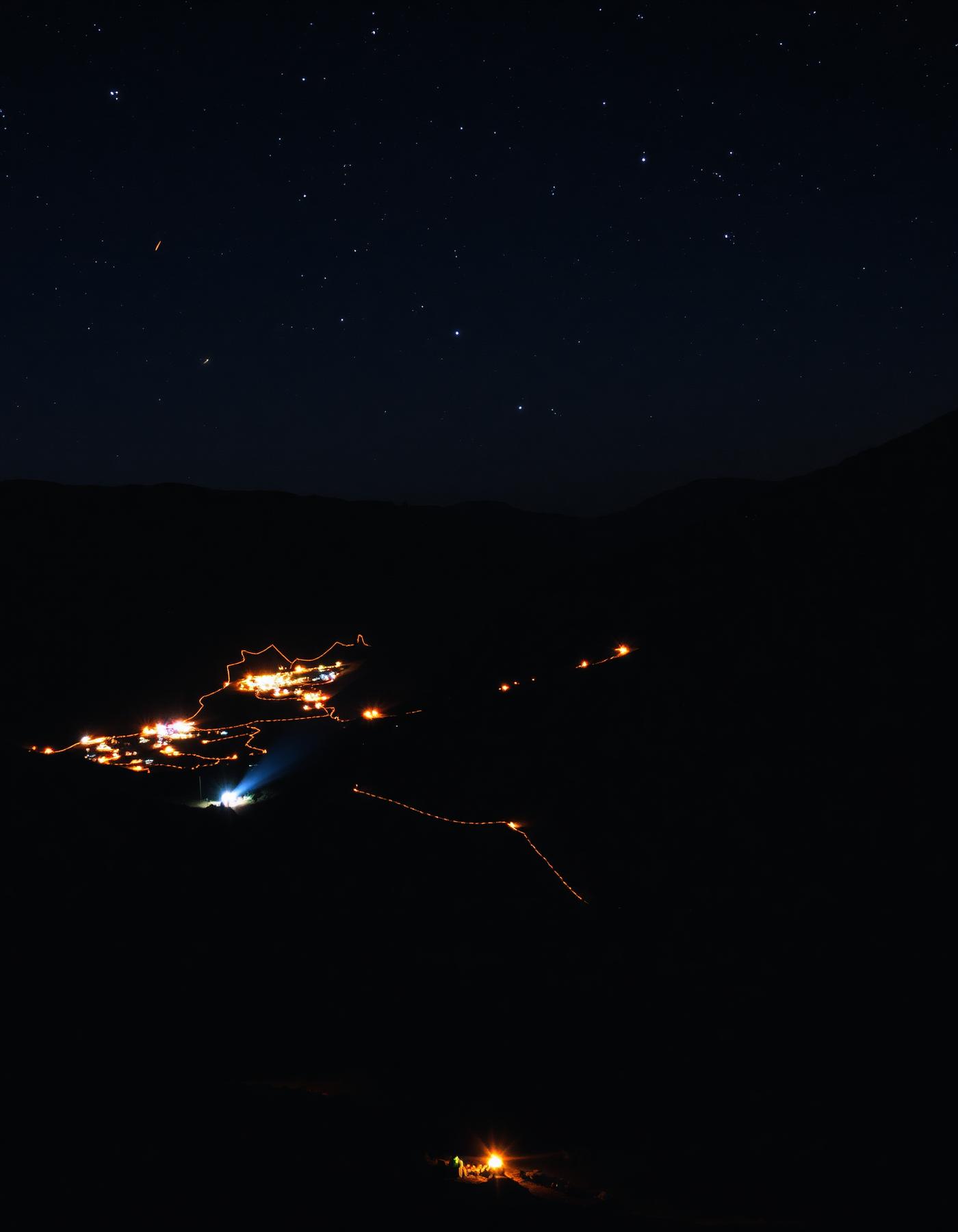 Distant camps and trails of light across a dark valley at night
